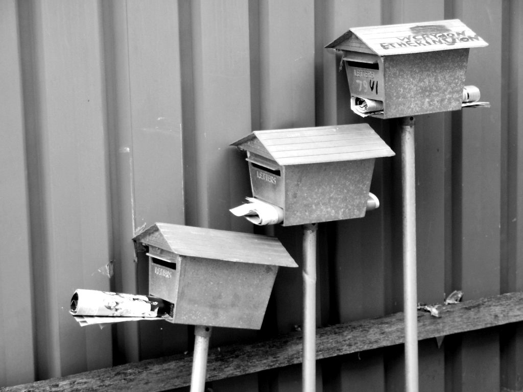 Three metal mailboxes on posts beside a wall