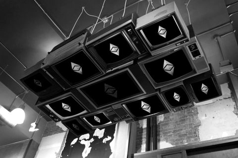 Ceiling-mounted screens each showing a diamond-shaped crypto logo