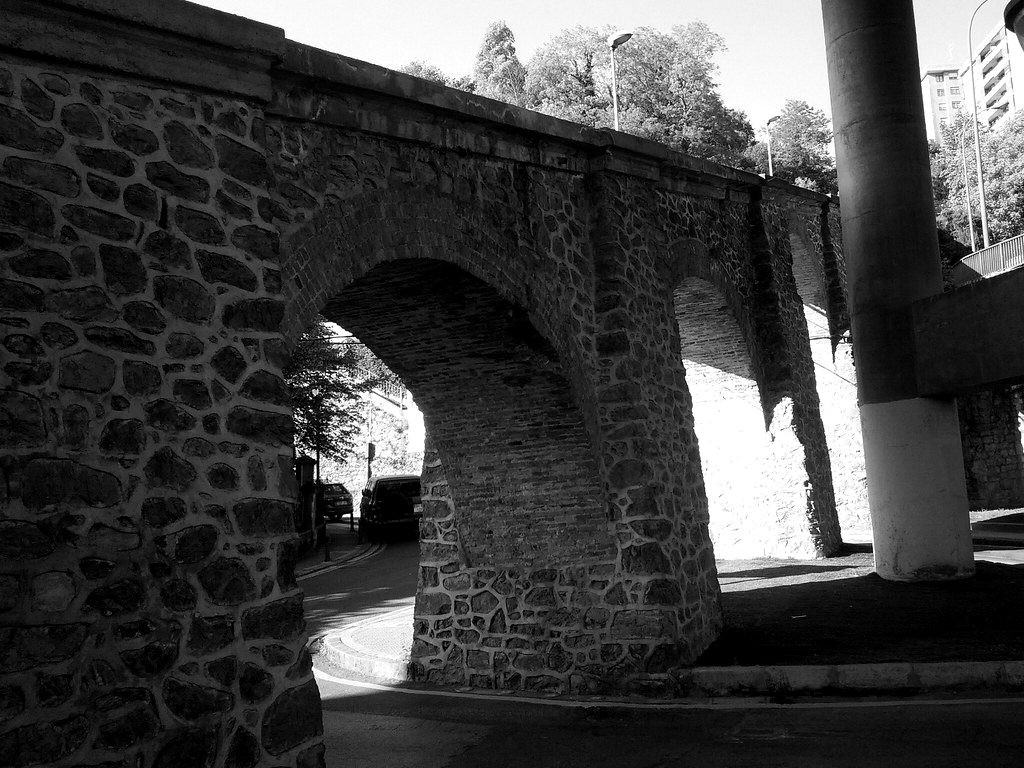 A stone arch bridge beneath a modern concrete flyover