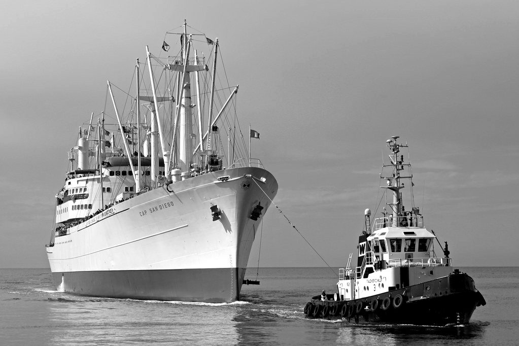 A tugboat guiding a white cargo ship