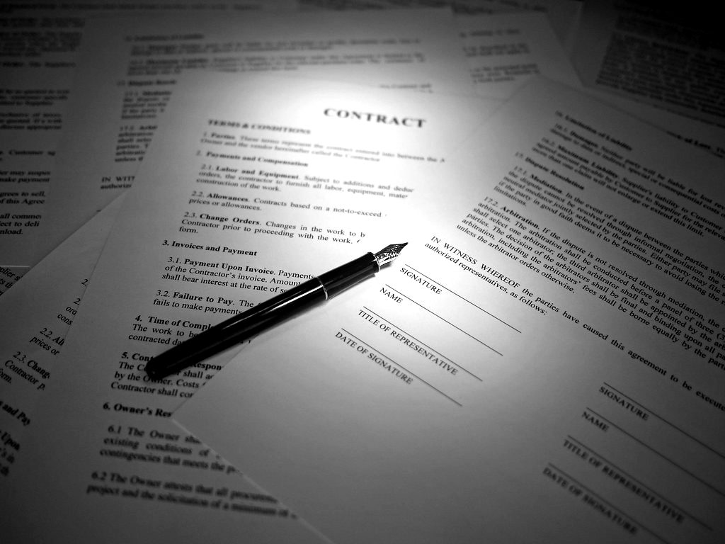 A fountain pen resting on a printed contract under a spotlight