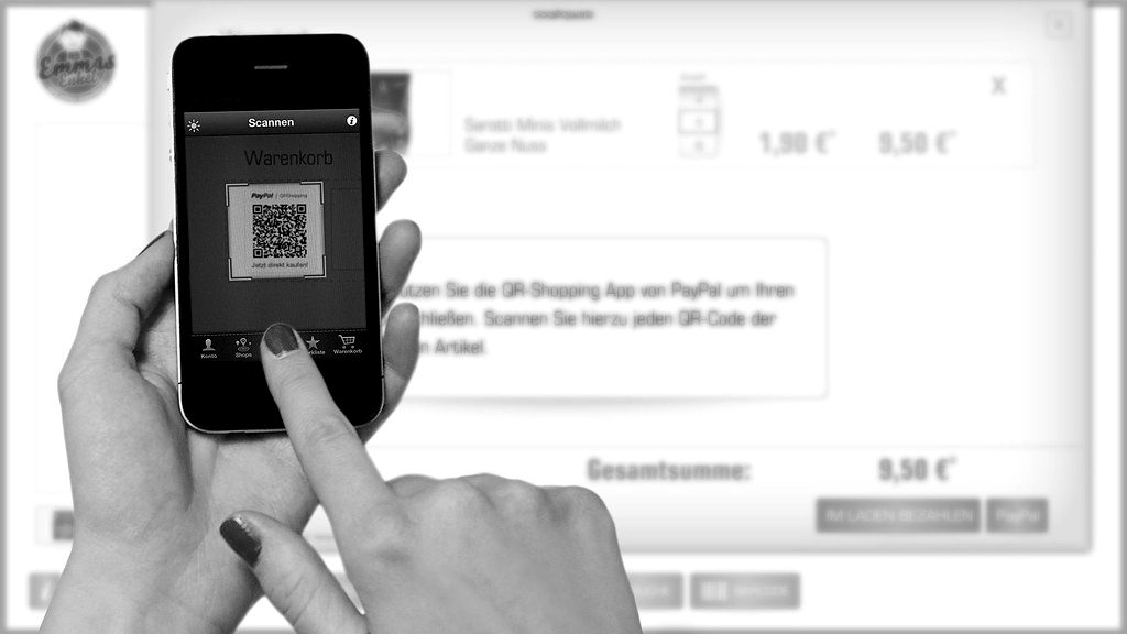 A hand holding a smartphone showing a QR code for payment