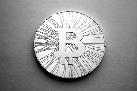 A gold-coloured physical Bitcoin token lying on a grey surface
