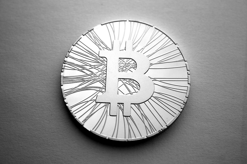 A gold-coloured physical Bitcoin token lying on a grey surface