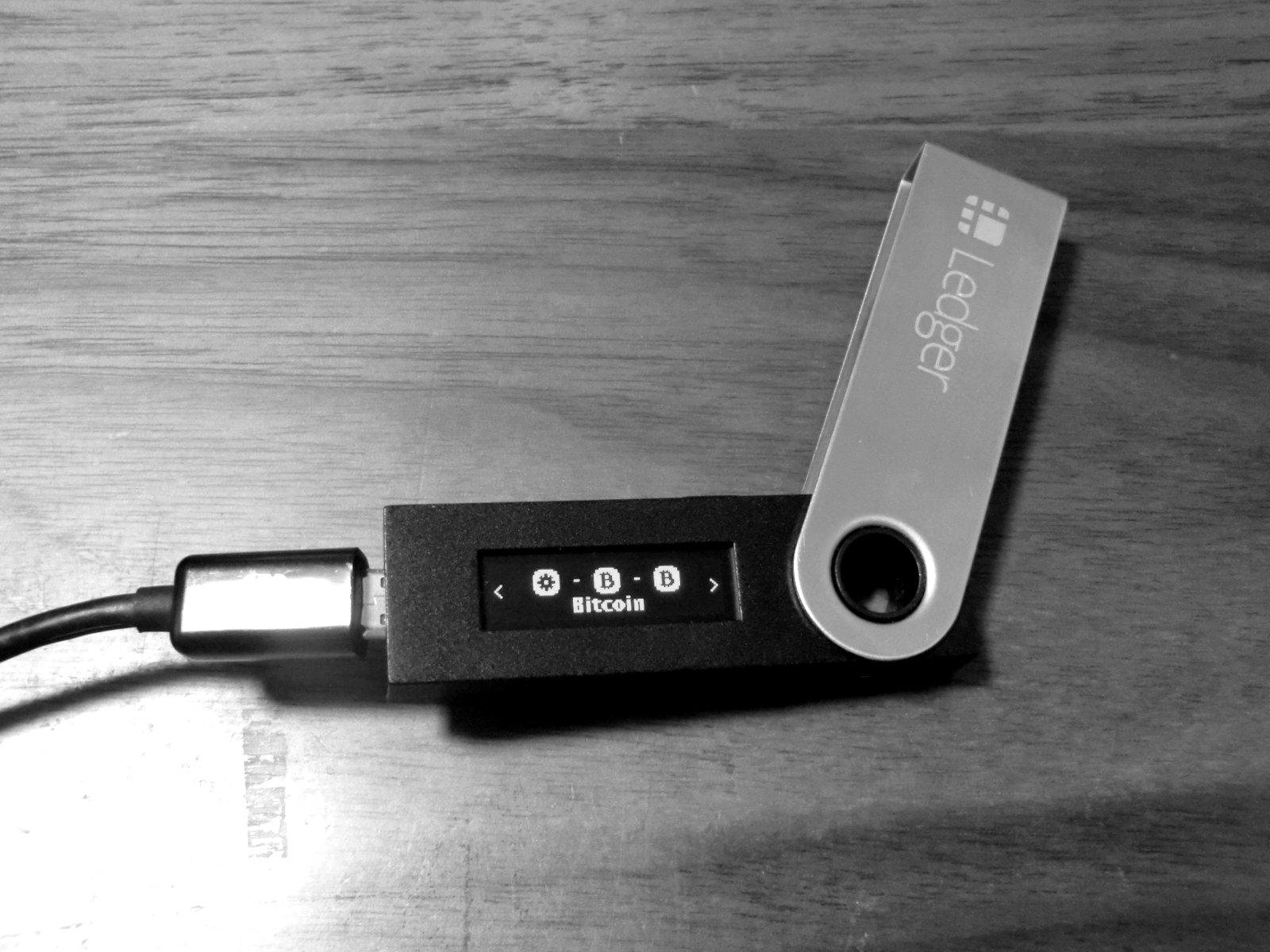 A hardware wallet connected to a cable, its small screen lit