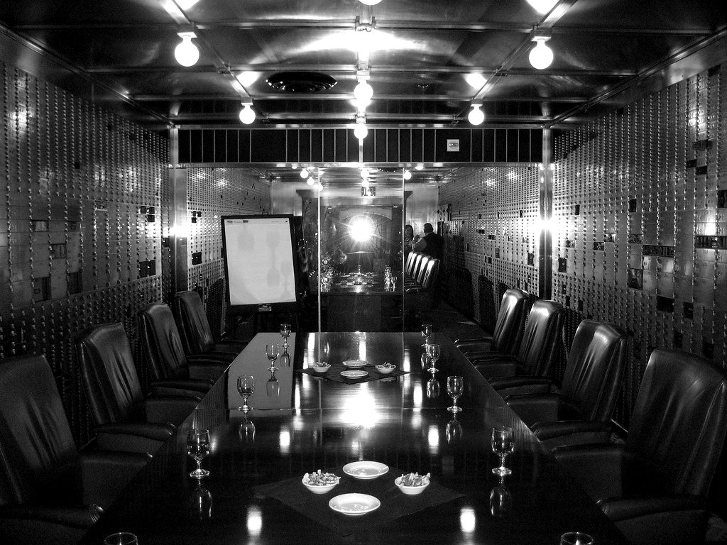 A conference table inside a vault lined with safe deposit boxes