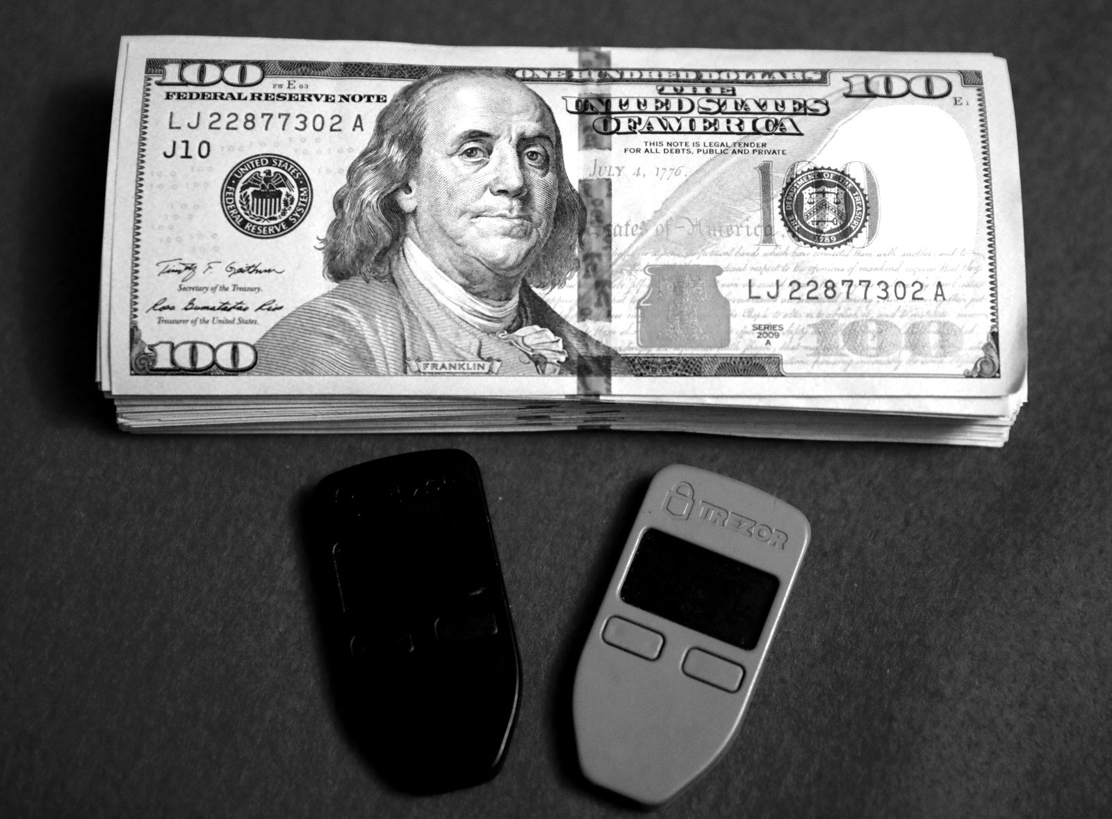 Two hardware wallets resting on a stack of US hundred-dollar bills