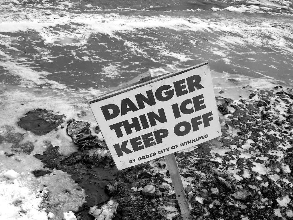A 'Danger thin ice, keep off' sign on a frozen shore