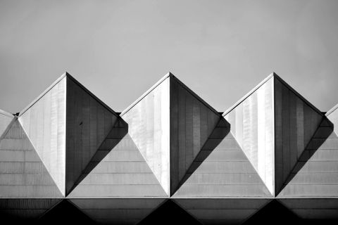 Three triangular concrete roof gables against a grey sky