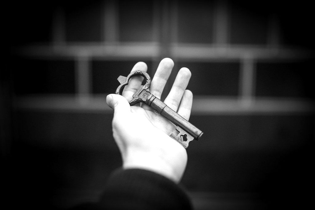 A hand holding an old iron key against a dark background