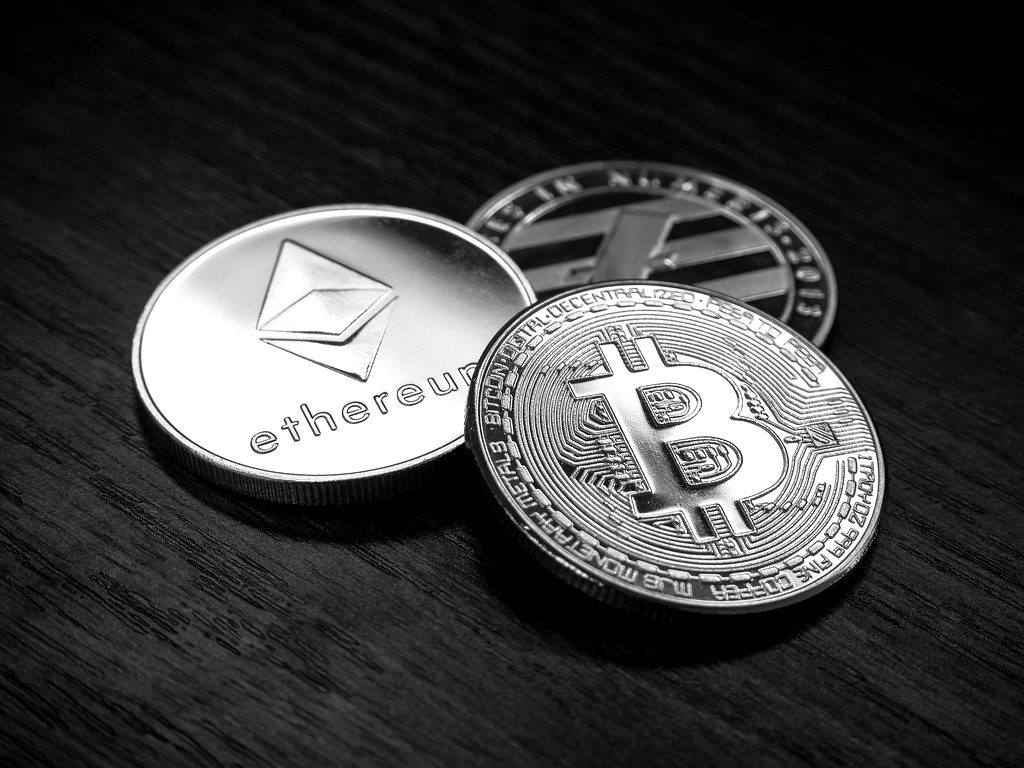Silver Ethereum and gold Bitcoin commemorative coins on a dark wooden table
