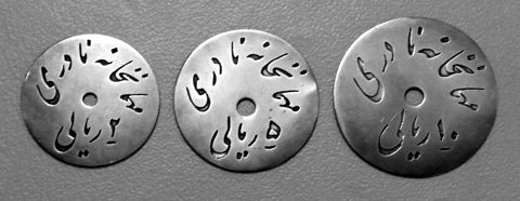 Three old silver tokens with Persian inscriptions on a green background